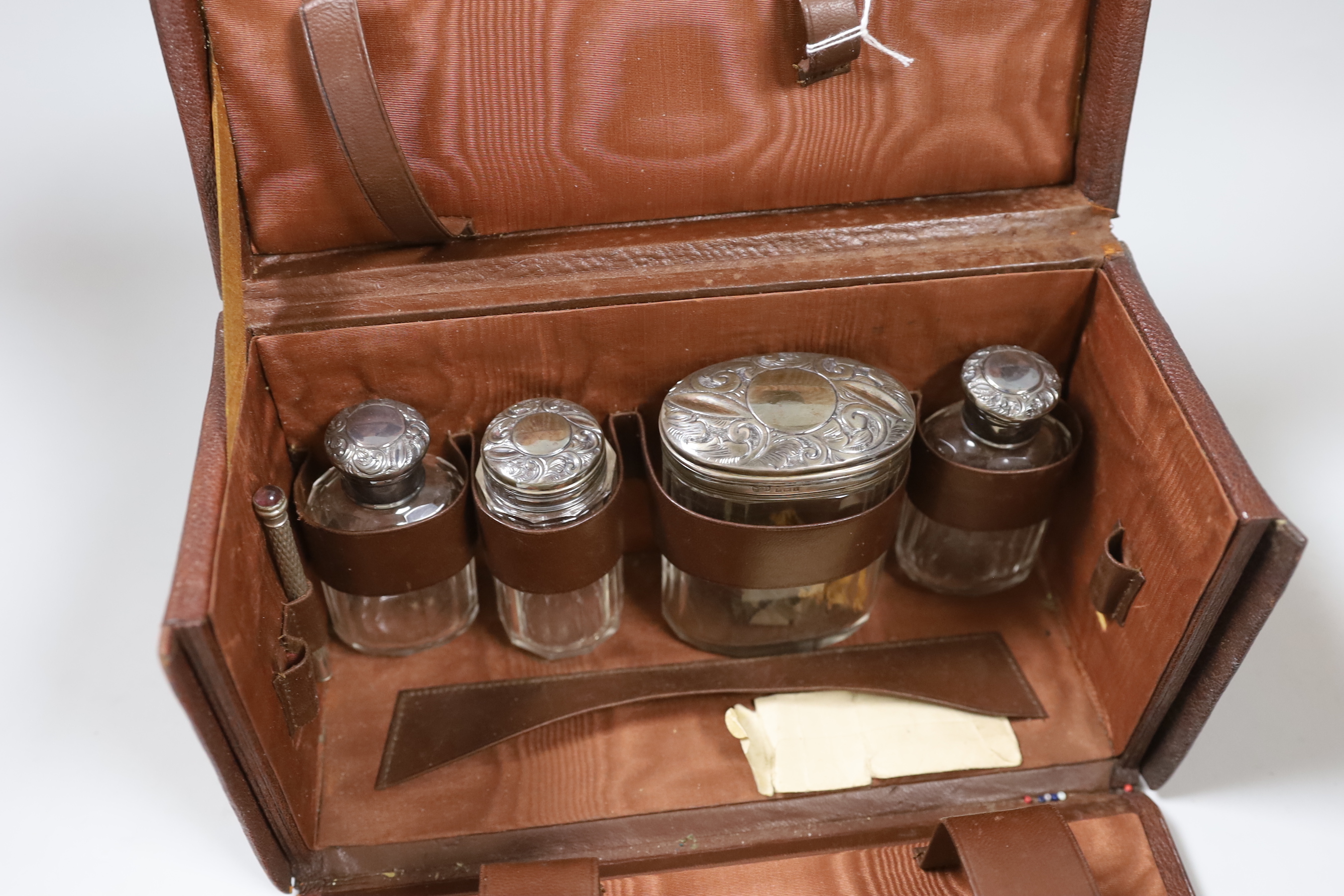 A George V leather travelling toilet case, containing five silver mounted glass jars, Birmingham, 1910, (incomplete), case 25cm.